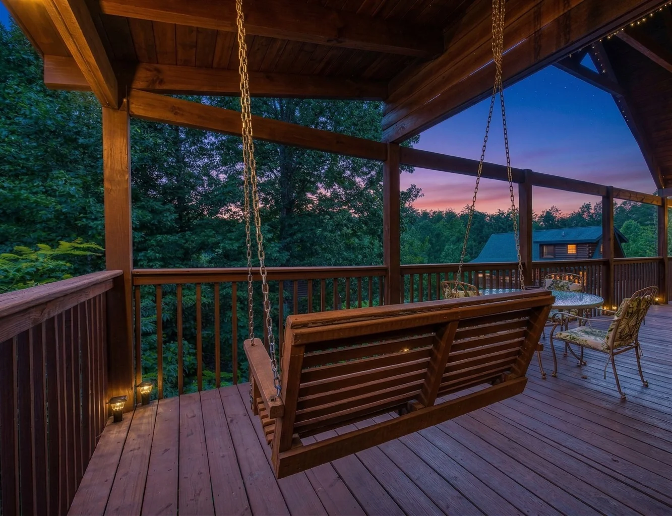 Rustic covered porch with wooden swing overlooking forested mountain sunset at best vacation rentals Gatlinburg