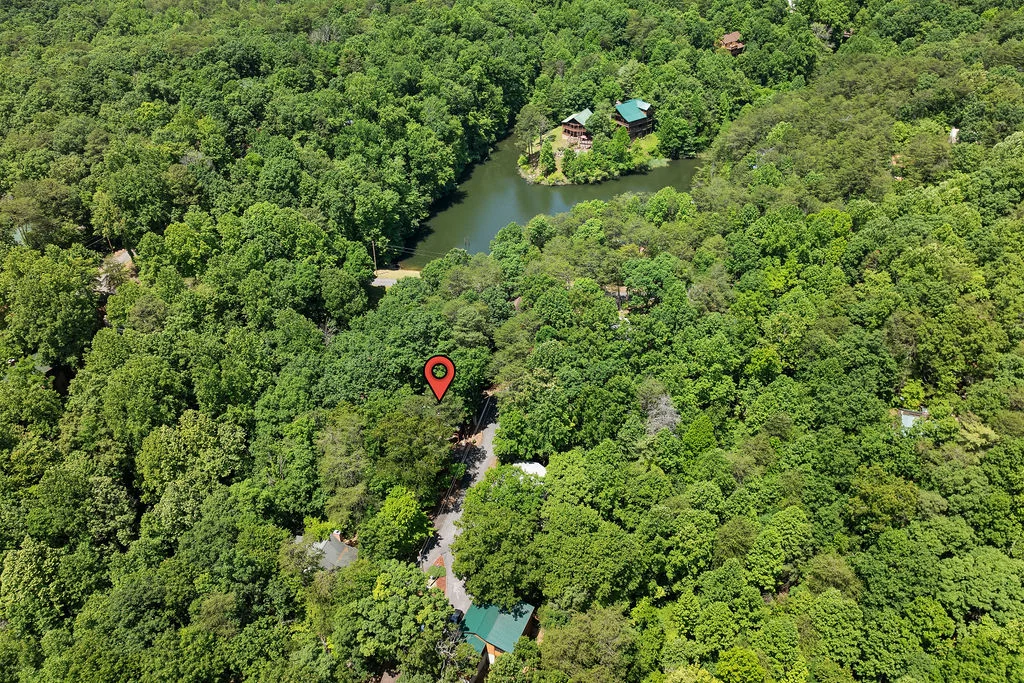 Aerial view of a cabin with blue roof nestled in forest with creek for pigeon forge property management
