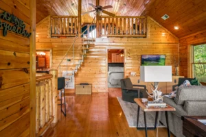 Open concept cabin interior with knotty pine wood, loft bedroom, and comfortable seating in a short term rental Sevierville,