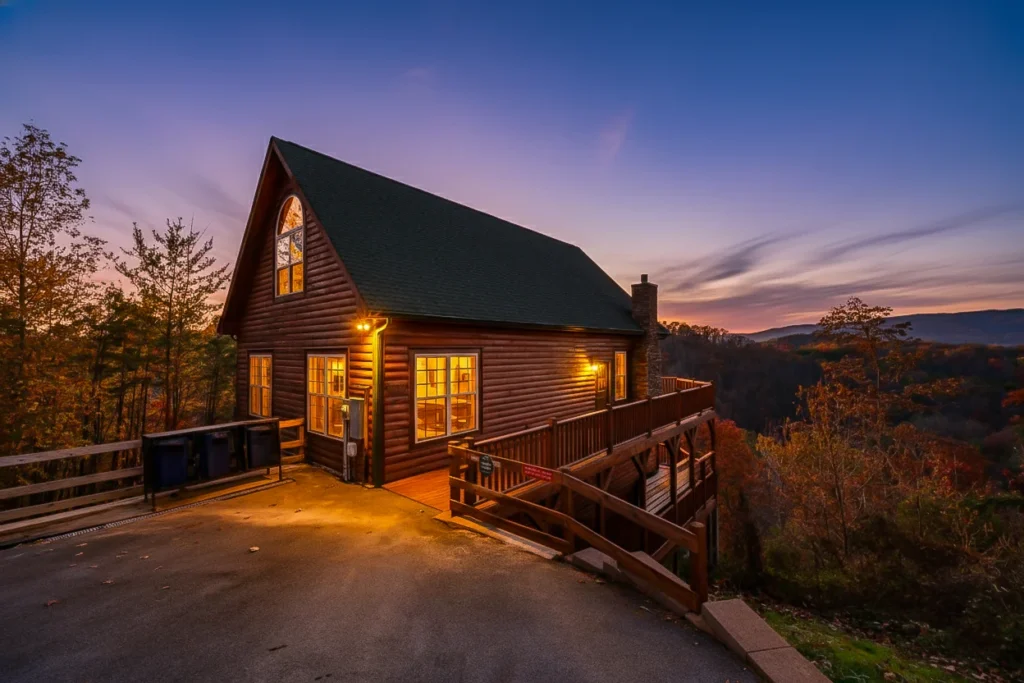 Log cabin rental in Pigeon Forge Tennessee with warm lighting, wooden deck overlooking forested mountains at sunset