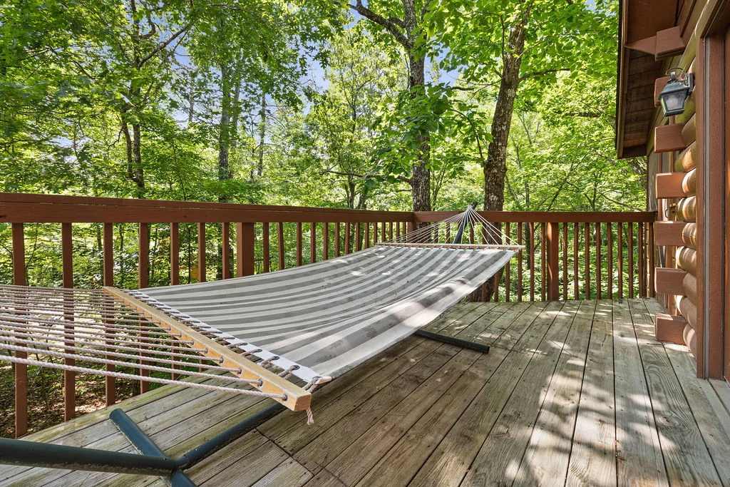 Striped hammock on wooden deck surrounded by forest trees in Sevierville cabin romantic getaway retreat