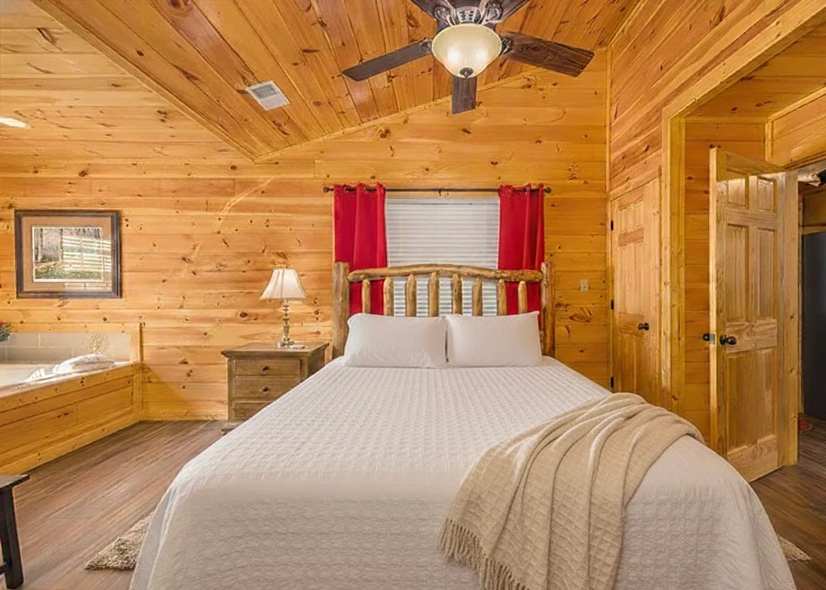 Rustic log cabin bedroom with knotty pine walls, queen bed, and jacuzzi tub in Sevierville TN