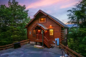 Log cabin with warm lighting and covered porch in Smoky Mountains rental at twilight in Sevierville