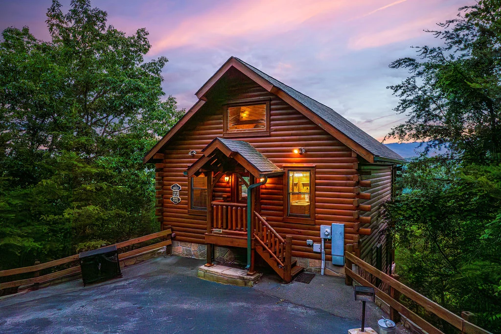 Log cabin with warm lighting and covered porch in Smoky Mountains rental at twilight in Sevierville