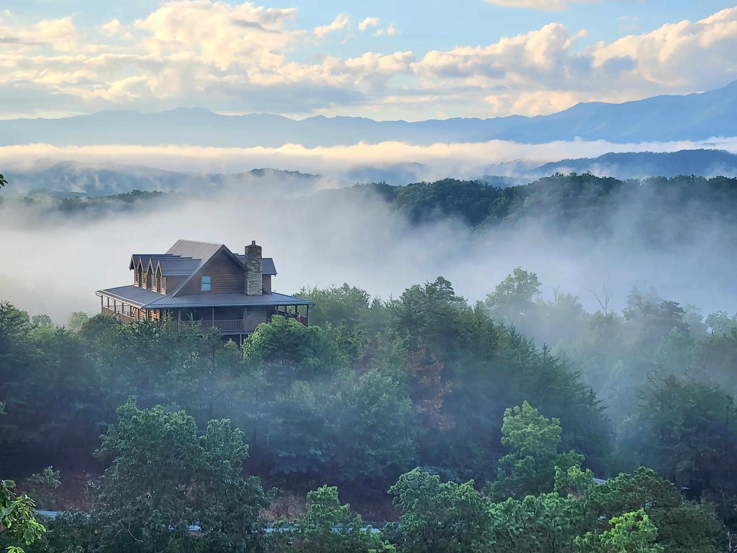 Elevated cabin with dark siding overlooking misty Smoky Mountains valley near Gatlinburg Tennessee at Hemlock Hills Cabin