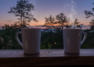 Two mugs with hot beverages on wooden railing overlooking misty mountains at sunset in Sevierville, TN