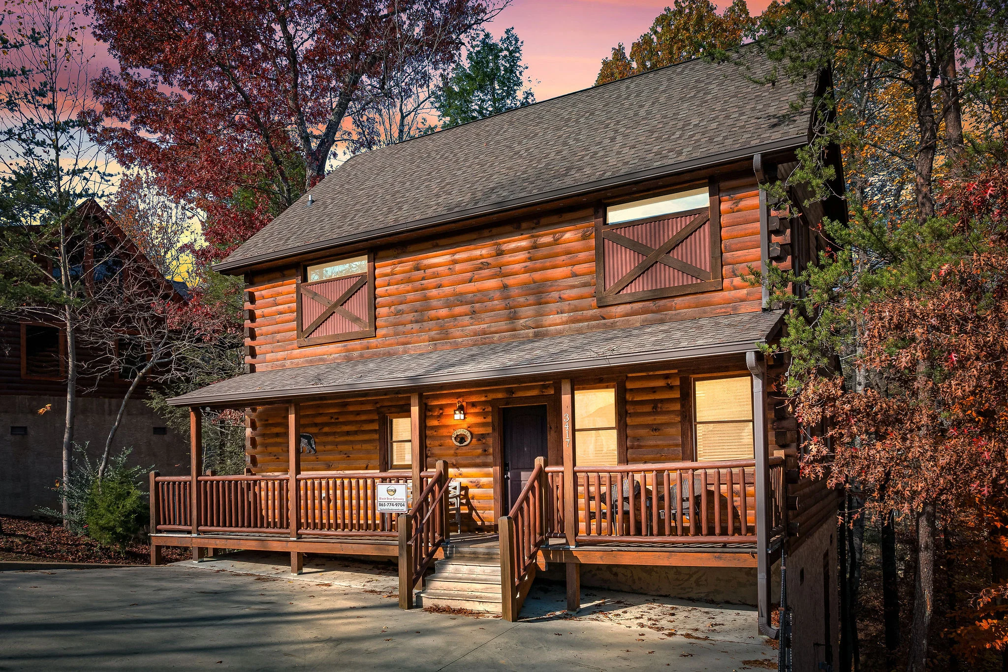 Two-story log cabin exterior with warm lighting and autumn foliage at sunset in Pigeon Forge