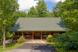 Log cabin exterior with wraparound front porch and gray shingled roof in green forest at 8 Bears Lodge, Gatlinburg, Tennessee