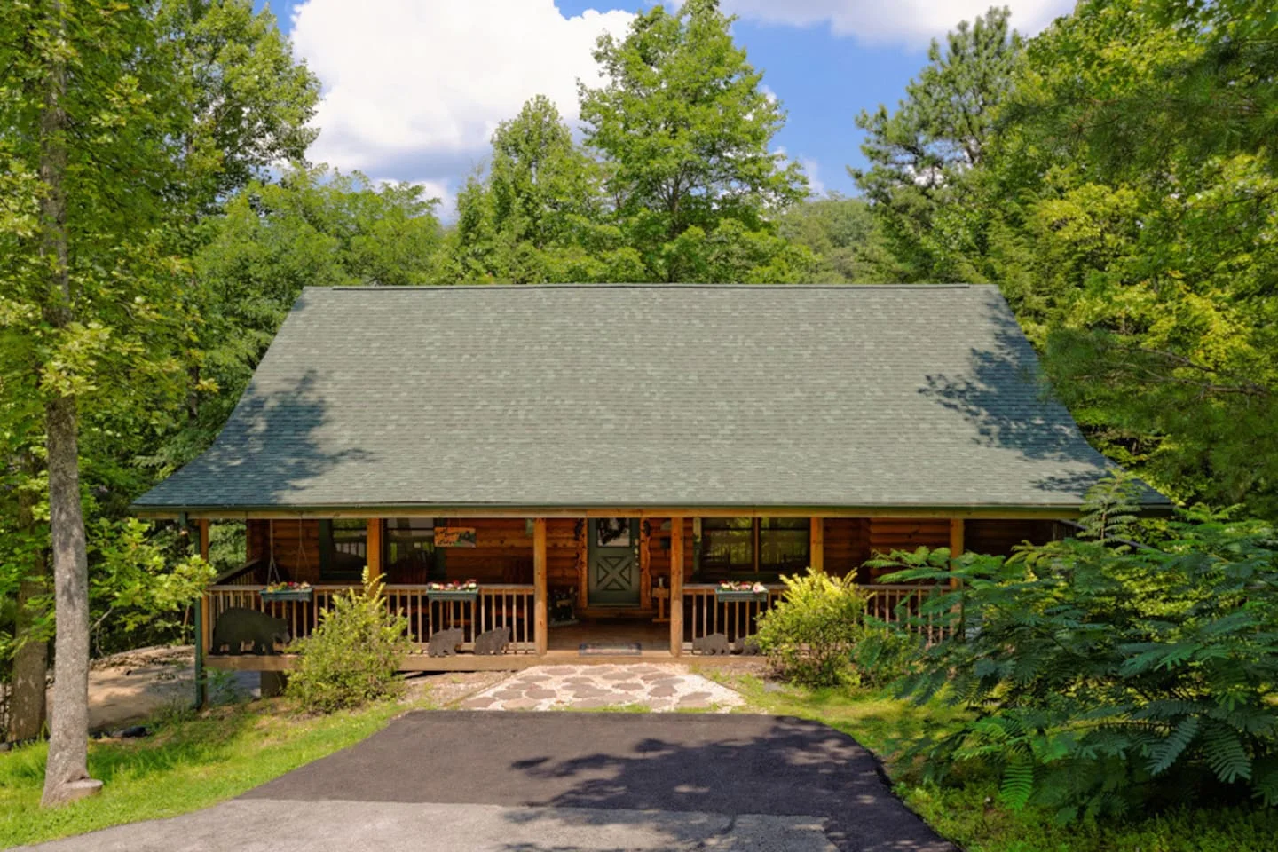 Log cabin exterior with wraparound front porch and gray shingled roof in green forest at 8 Bears Lodge, Gatlinburg, Tennessee