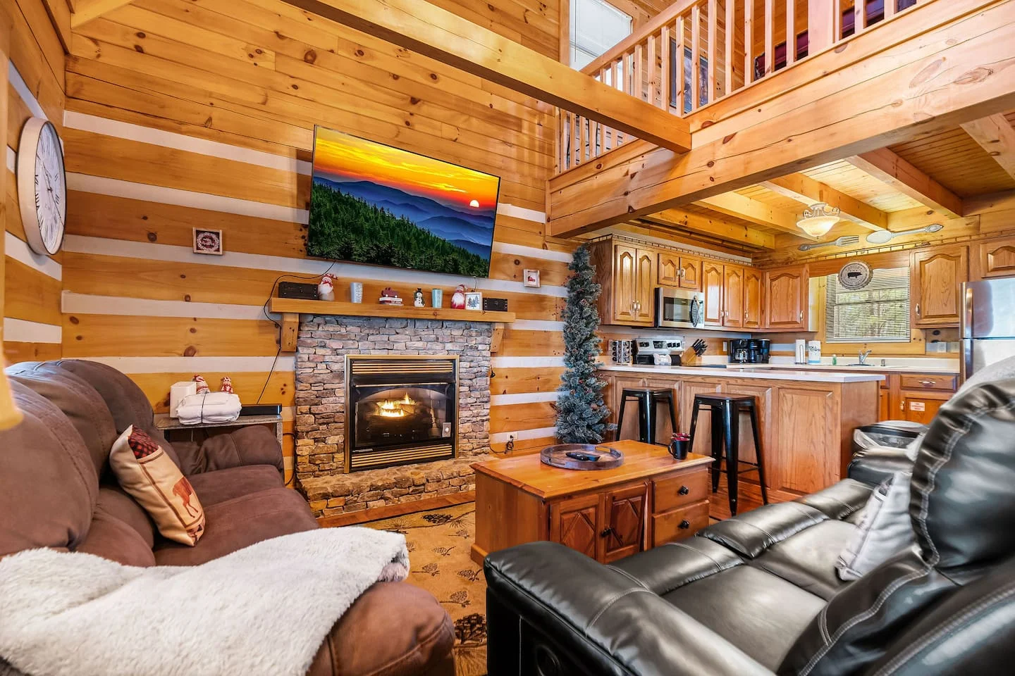 Cozy log cabin living room with stone fireplace, leather recliners, and open kitchen, ideal for an NYE celebration in our