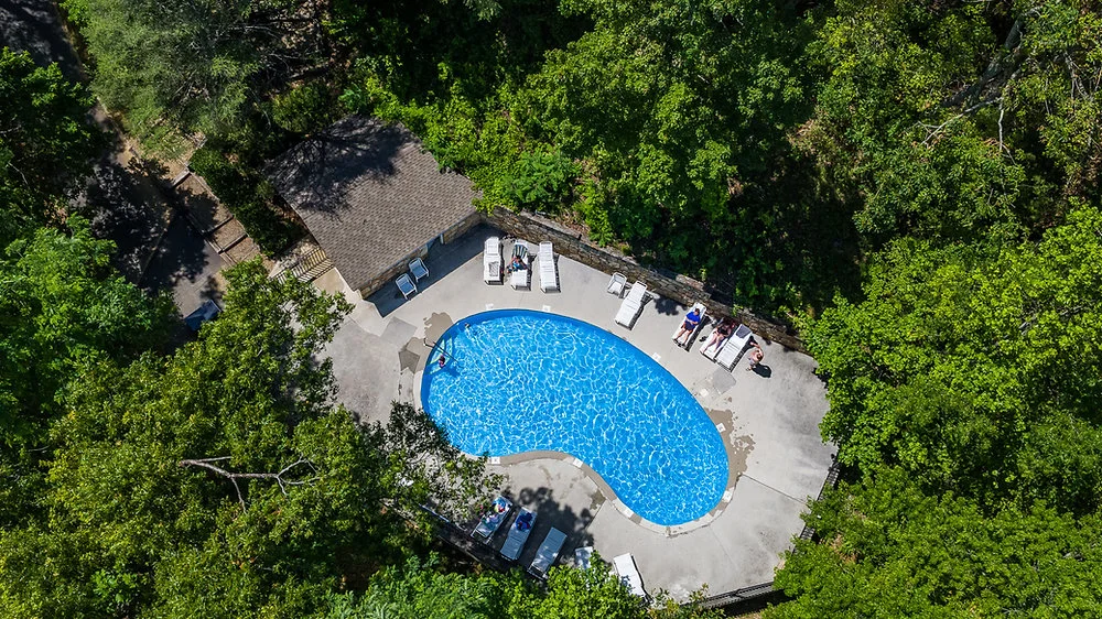 Aerial view of kidney-shaped resort pool surrounded by lounge chairs and pavilion in forest setting near Gatlinburg