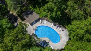 Aerial view of a kidney-shaped blue resort pool with lounge chairs in a forest setting at Serene Escape, Gatlinburg,