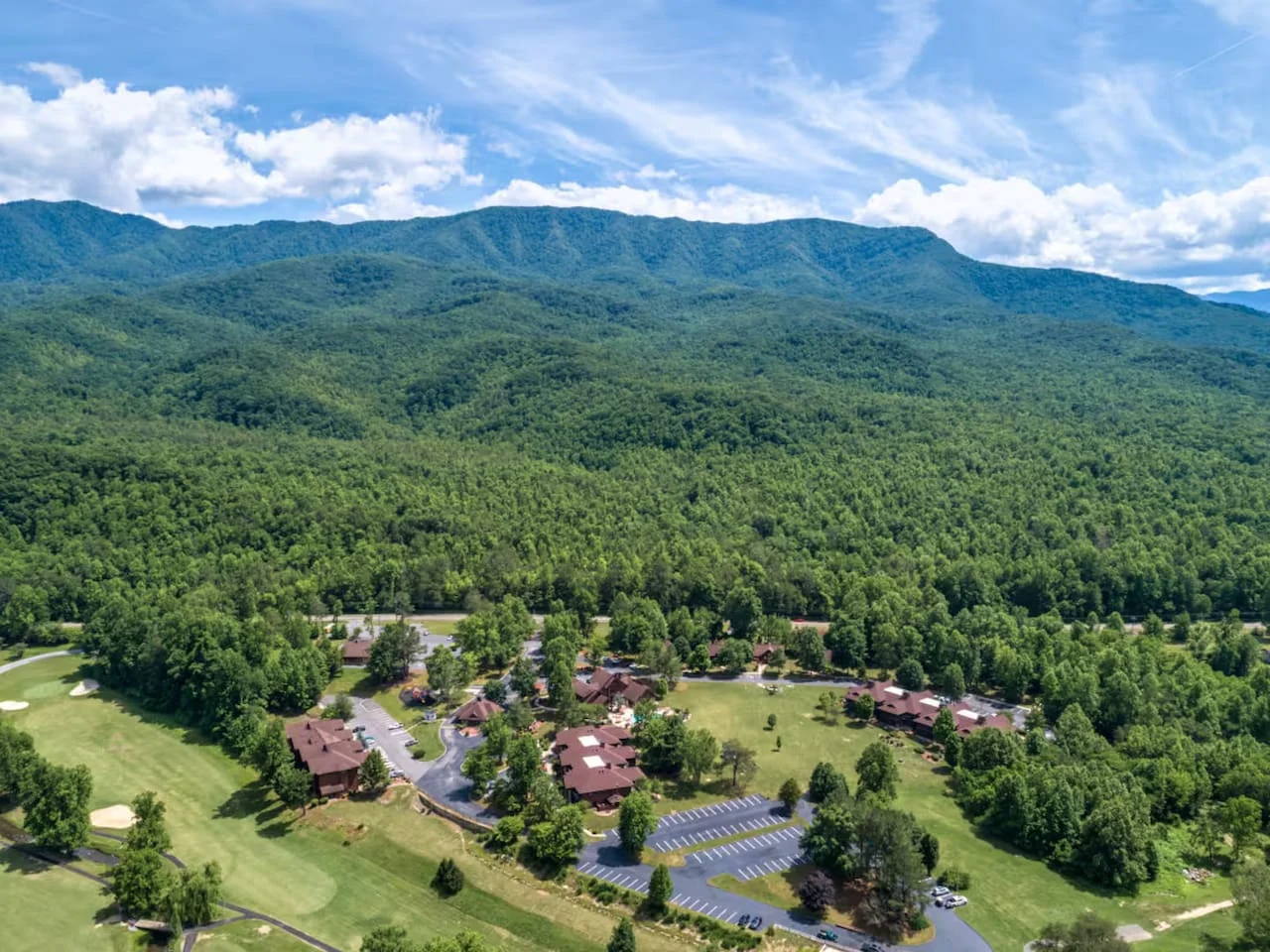 Aerial view of a resort community with log cabins in a forested valley under Smoky Mountain ridges, a Gatlinburg TN July